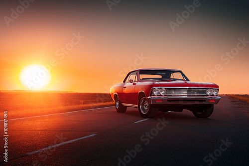 Retro red car standing on asphalt road at sunset