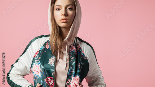 Fashionable beautiful young woman in a bomb jacket with floral print stands on a pink background