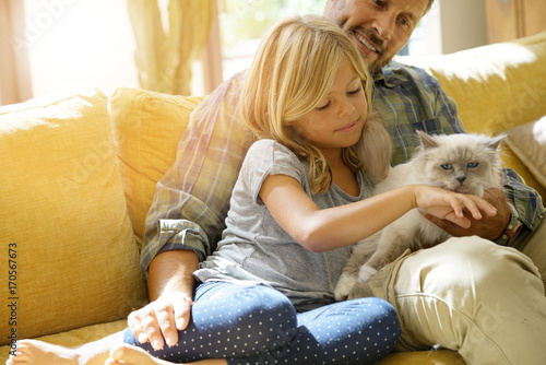 Daddy with little girl petting cat sitting on sofa