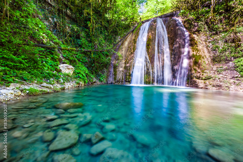 Waterfall in a green spring forest surrounded by stones, clear turquoise water on an impressive natural landscape. 33 Waterfalls, Sochi, Russia.
