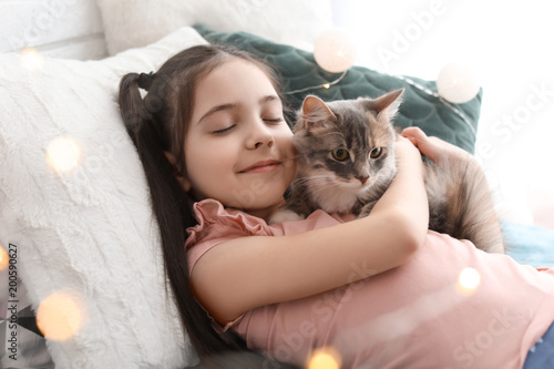 Cute little girl with cat lying on bed at home