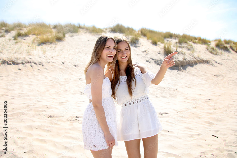 Zwei H Bsche Blonde Frauen In Weissen Kleidern Stehen Lachend Am Strand Eine Frau Zeigt In Eine