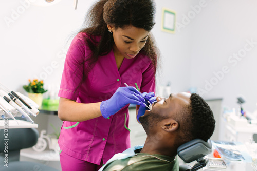 Female dentist examining a patient with tools in dental clinic. Doctor doing dental treatment on man's teeth in the dentists chair.