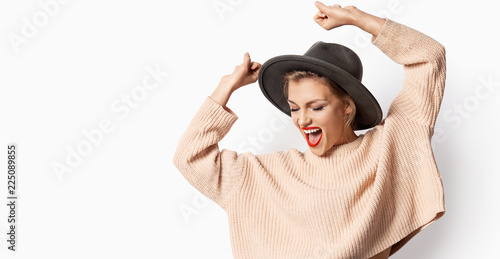Portrait of beautiful smiling girl in hat and wearing knitted sweater on white background. Woman with bright emotion. Autumn fashion concept.