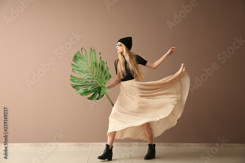 Beautiful woman with green tropical leaf near color wall