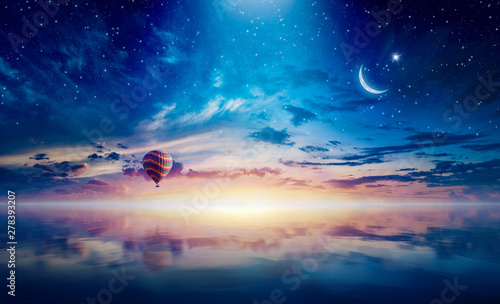 Crescent and hot air balloon rising above serene sea in sunset glowing sky