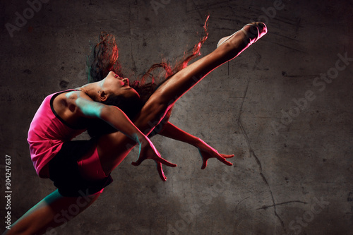 Street dance girl dancer jumping up dancing in neon light doing gymnastic exercises 