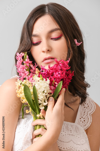 Beautiful young woman with hyacinth flowers on light background