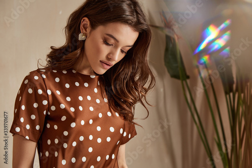 Portrait of beautiful woman fashion model brunette hair wear brown silk dress accessory jewelry earrings cosmetic face clothes for romantic date party walk summer collection tanned skin green leaves.