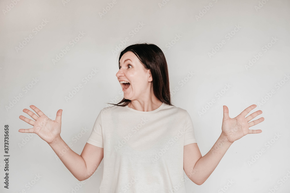 Emotional Brunette Woman With Surprised Face Keeps Holds Hands To The Side Dressed In Casual