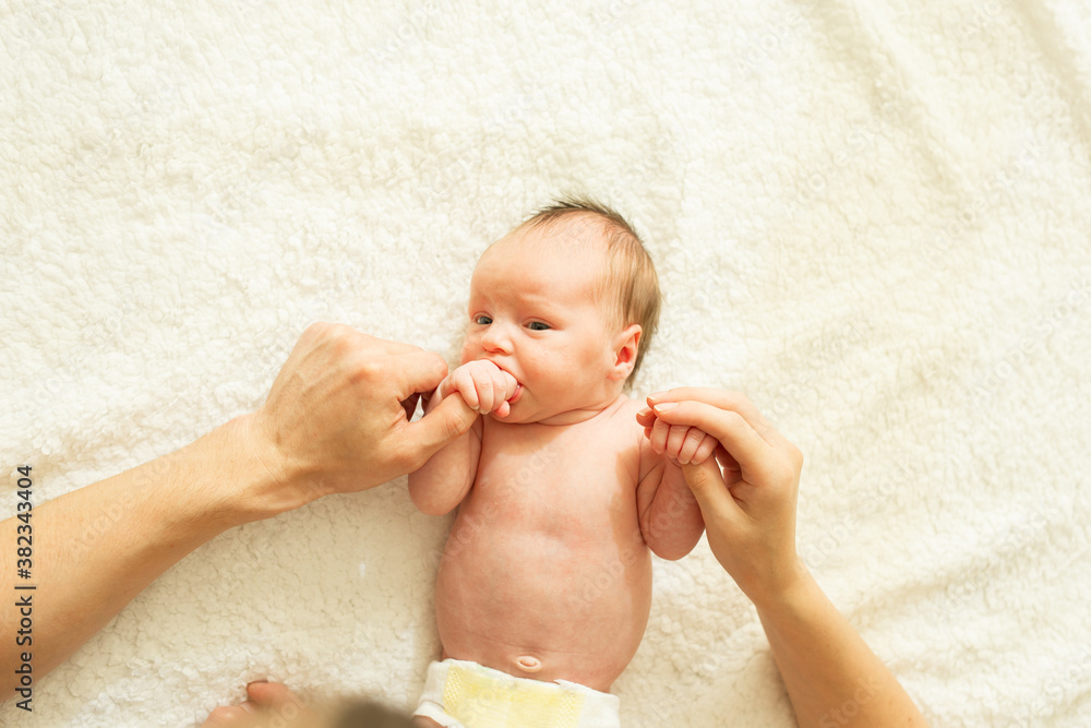 Cute Naked Newborn Baby With Open Eyes Lying On A Bed A Parent Holds The Legs Of A Newborn
