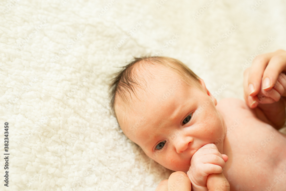 Cute Naked Newborn Baby With Open Eyes Lying On A Bed A Parent Holds The Legs Of A Newborn