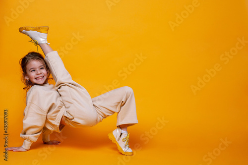 Cute little girl dancing on a yellow background. Space for text.