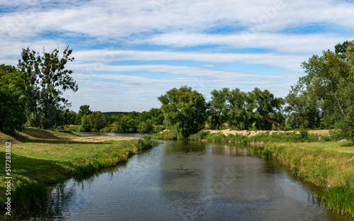 krajobraz rzeki Osobłogi w zachodniej Polsce w jasnych zielono niebieskich barwach i lekko pochmurnej pogodzie