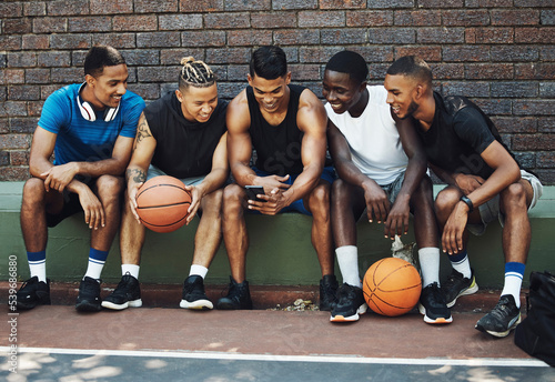 Basketball friends, rest together with phone and relax watch a funny video on smartphone after training on sports court. Healthy men, relax and tired on bench after workout game for fitness exercise