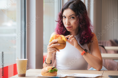 Frowned disgruntled girl customer of a fast food restaurant digs into a burger and found a spoiled product in her lunch