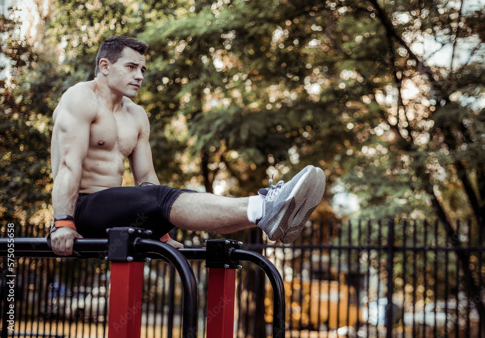Athletic Male Athlete With A Naked Torso Trains The Abdominal Muscles By Lifting His Legs Up On