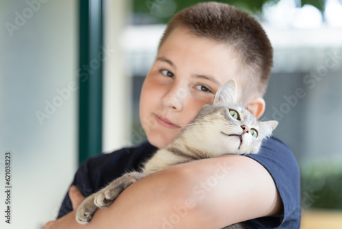 close-up of teenager looking at camera. Boy holding and gently hugging his tabby cat outdoors near home