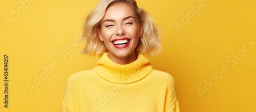 Blonde woman with white teeth happy expression and dressed casual poses for promotion on yellow background