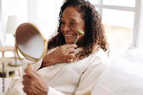 Senior black woman massaging her face with a jade roller