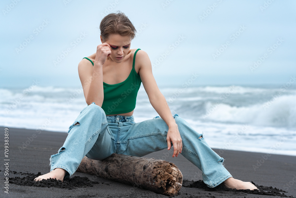 Blonde Woman Sitting On Log With Her Legs Spread And Head Lowered Thoughtfully Looking Down On