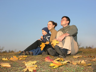 family sit with autumn leaves