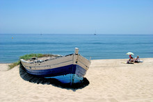 Old Rowing Boat On White Sandy Beach And People Sunbathing Next