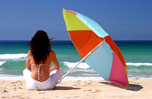 Woman Sitting Under Colorful Parasol On White Sandy Beach