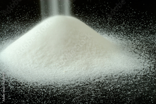 Fotografie, Obraz sugar falls on a mountain of granulated sugar on a black backgro