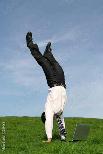 Fotografia businessman doing handstand and using laptop outdo