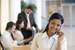 © carlosseller - Business woman on headset with seated working colleagues hehind