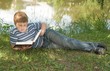 © StepStock - A little boy reads a big book with river at background