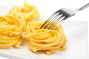 A uncooked pasta nests and fork on a dish on white background