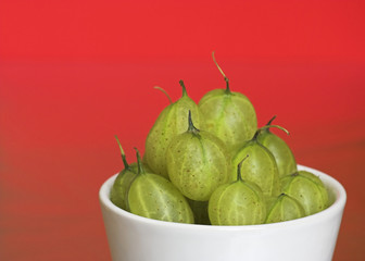 Wall Mural - Bowl of Gooseberries on a Red Background