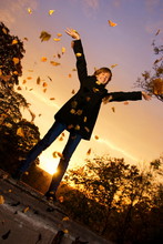 Young Girl Throwing Autumn Leaves At Sunset Time