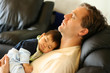 Father sleeping on chair with his baby boy on chest