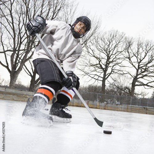 Photo Boy in ice hockey uniform skating on ice rink moving puck.