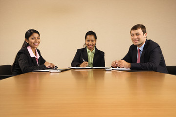 Businesspeople sitting at conference table smiling.