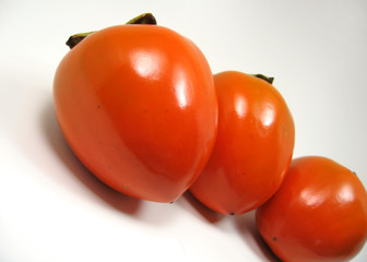 three organic hachiya persimmons in a row isolated on white.