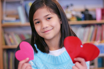 Wall Mural - Nine year old girl holding up two red hearts.