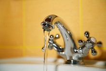 Working Water Tap. Flowing Water. Selective Focus, Shallow Depth Of Field. Blurred Yellow Tiled Background