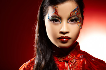 Beautiful Asian girl as a plastic doll on red background