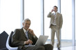 © carlosseller - Mature businessman seated with laptop and colleague on phone