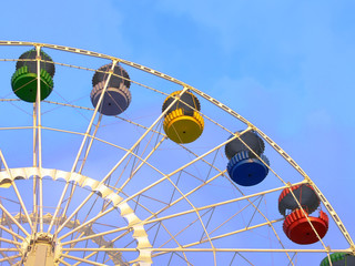 Big ferris wheel with colorful cabins on blue sky