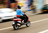 Fototapeta Krajobraz - Panning shot of a young girl riding a scooter in a European city