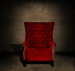 A grungy red velvet chair in a dark room