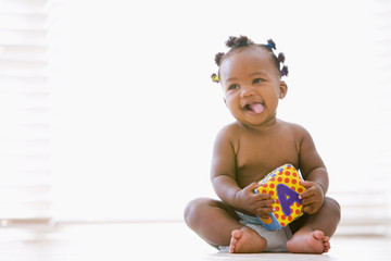 Baby sitting indoors with block smiling