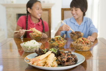 Two young children eating chinese food in dining room smiling