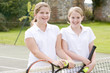 © Monkey Business - Two young girl friends with rackets on tennis court smiling