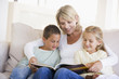 © Monkey Business - Woman and two children sitting in living room reading book and s